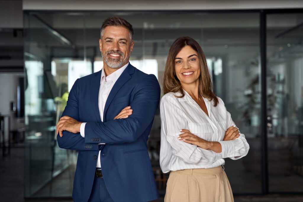 Business professionals stand confidently in a modern office setting, smiling and posing with arms crossed, showcasing teamwork and leadership.