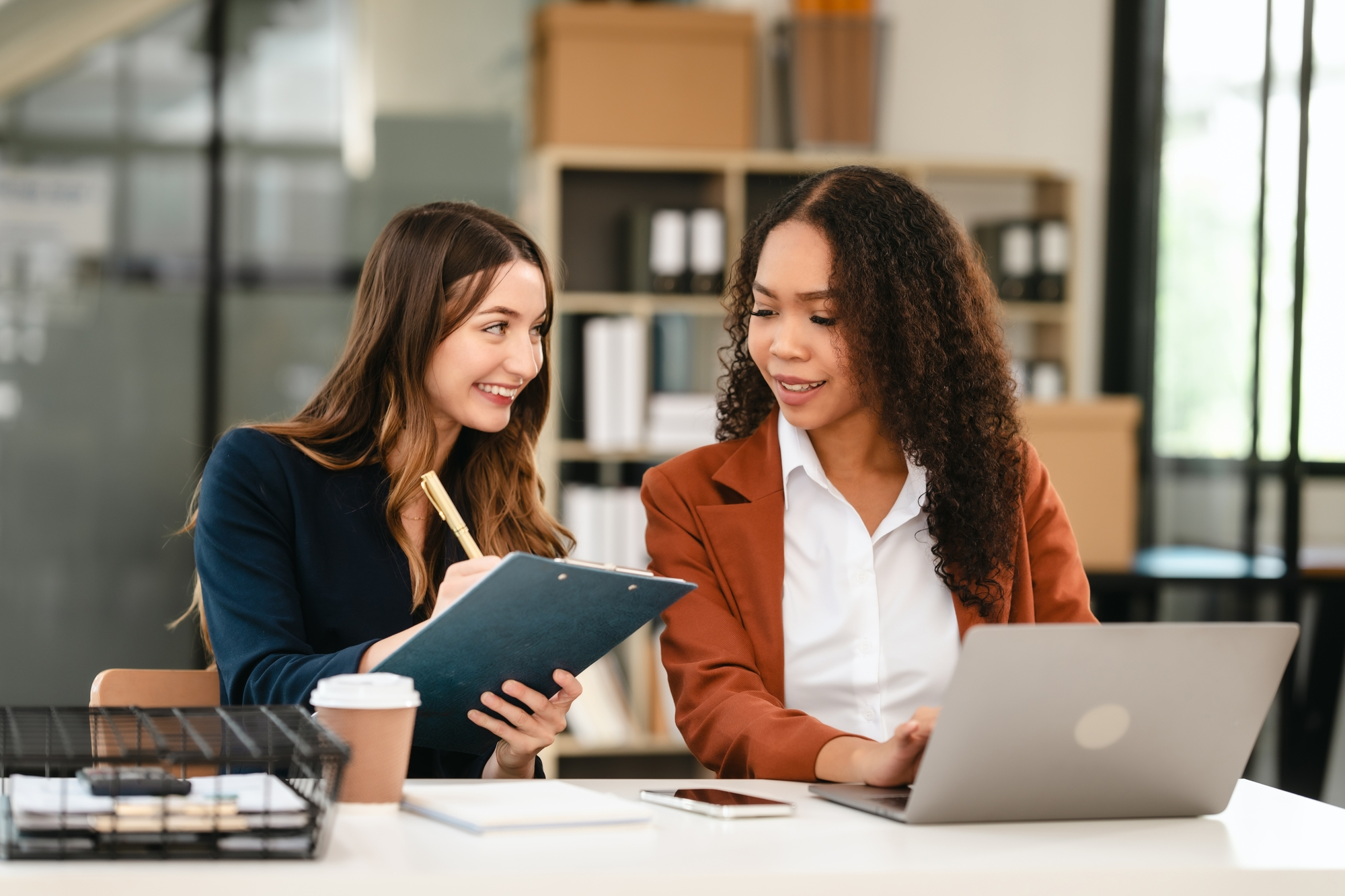 Two professional caucasian with african american businesswoman friends collaboration, working together at office, using laptop